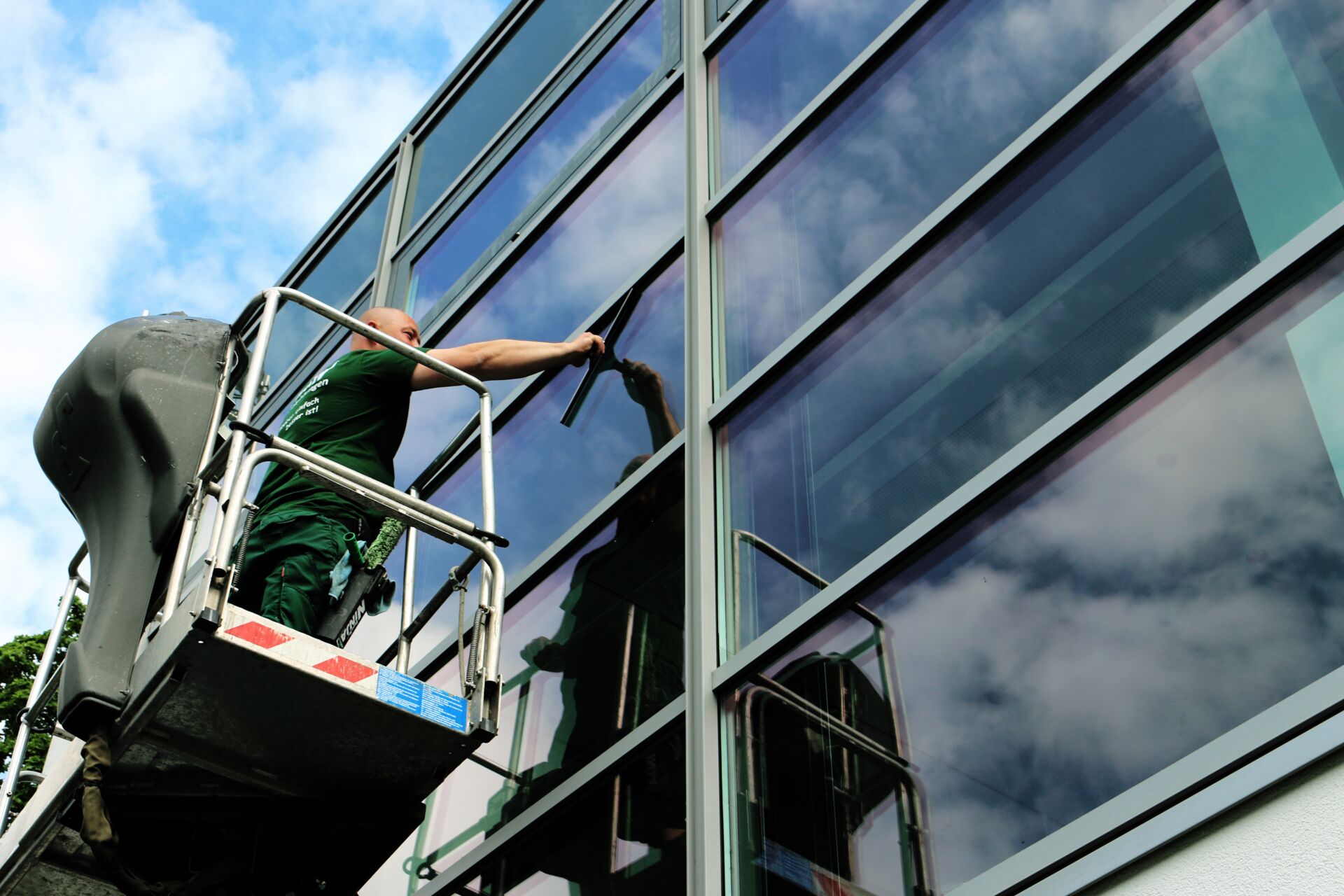 Eine Person reinigt Fenster an einem Gebäude von einer Leiter aus