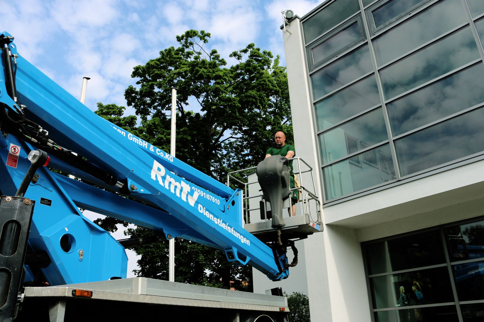 Ein Mitarbeiter auf einer blaue Arbeitsbühne vor einem Gebäude, mit der Aufschrift RmTV.
