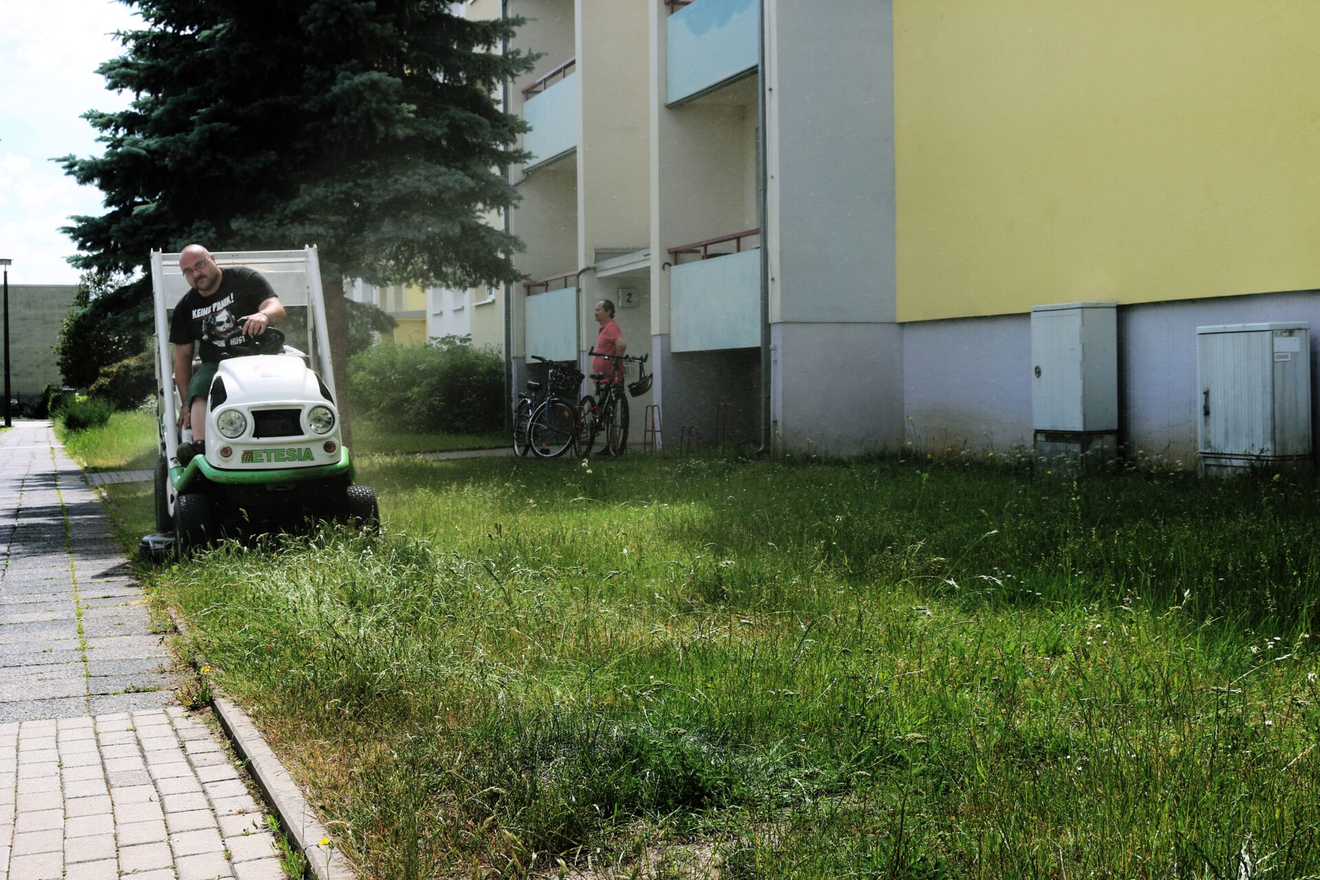 Ein Mitarbeiter mäht Gras vor einem Gebäude mit einem Rasenmäher
