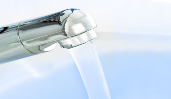 Ein sauberer Wasserhahn vor einem blauen Hintergrund, wo Wasser rauskommt.